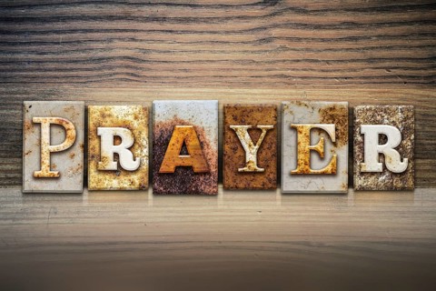 The word PRAYER written in rusty metal letterpress type sitting on a wooden ledge background