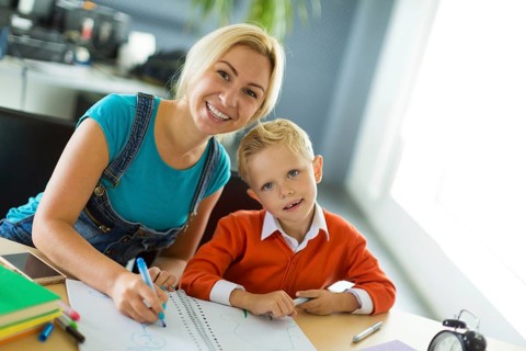 Young blonde caucasian kid in orange shirt and his mother sit at the table with colorful folders