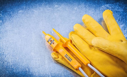 Yellow electrical tester protective gloves on metallic background electricity concept