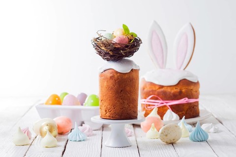 In the foreground an Easter cake decorated with a nest on the top. Painted eggs in the nest. In the
