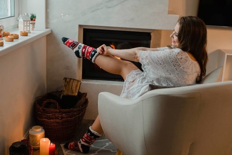 The young girl is sitting in a cozy room by the fireplace. The girl is sitting in an easy chair and