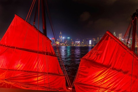 Close up of red-sail junk boat with Hong Kong island skyline background seen from the waterfront of