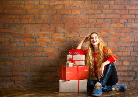 Young woman with Christmas gift near brick wall