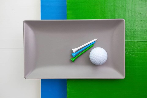 Gray ceramic dish with golf equipments on over white, blue and green wooden table, rectangle dish