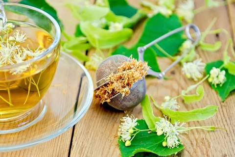Metal sieve with dried flowers of linden, fresh linden flowers, tea in a glass cup on a wooden