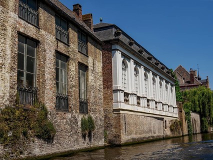 Historic buildings with brick façade along a canal, partly surrounded by greenery, under a clear