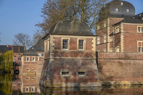A pavilion and a brick castle reflected in the calm waters of a moat, ahaus, münsterland, germany