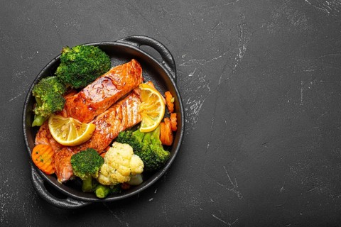 Healthy baked fish salmon steaks, broccoli, cauliflower, carrot in cast iron casserole bowl black