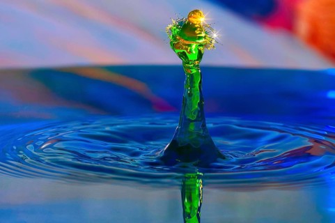 A drop of water in bright green creates a lively splashing movement on a blue water surface,