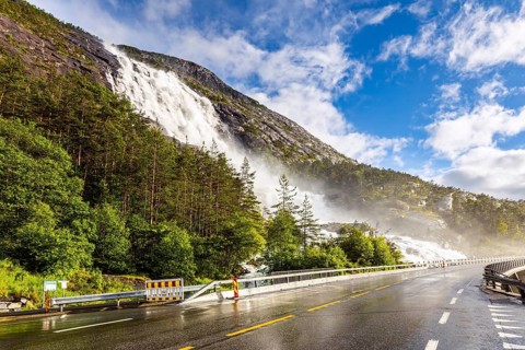 Summer cold day. The cascading Langfossen waterfall picturesquely intersects with the highway and