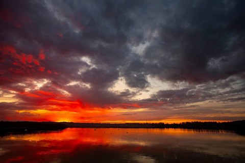 A truly stunning sunset over a calm and reflective lake showcases vibrant hues and dynamic clouds