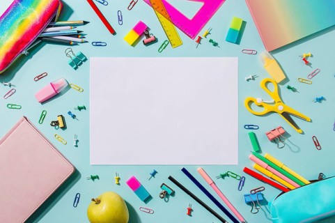 Creative student desk with empty white sheet and colorful modern school supplies on blue background