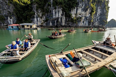Tourists in boats enjoy a ride along a rocky shore, rowing boats for tourists in Halong Bay in