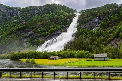 Norway. Huge powerful waterfal Vidfossen. White water foam envelops the foot of the waterfall. Lush