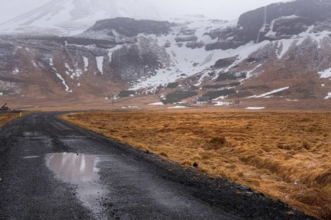 Empty rural road leading to a snowcapped mountain. Icelandic landscape