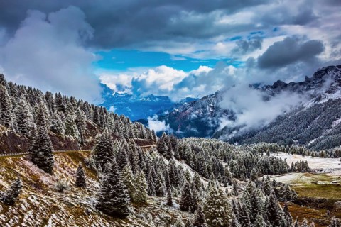 Heavy rain clouds flying over mountains. Evergreen forests in the valley covered with the first