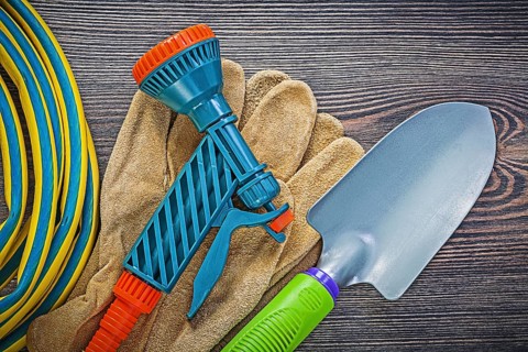 Coiled garden rubber hose leather safety gloves hand shovel on wood board gardening concept