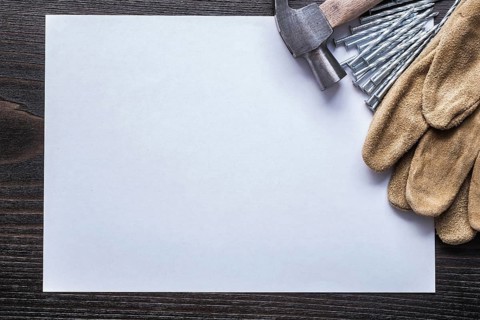 Sheet of paper metal nails claw hammer and leather safety gloves on vintage wooden board copy space