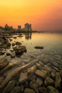 Castle ruins at dawn. Bay on the Mediterranean Sea with calm water at sunrise. Reflection of the