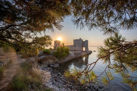 Sunrise on a rocky coast. Reflection in the calm water. Landscape shot of the restored remains of