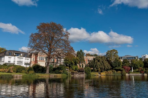 Stylish townhouses reflected in the water, surrounded by lush autumn foliage, Alster, Hamburg,