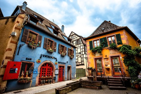 Colourful historic facades with cosy bars and restaurants under a cloudy sky. Alsace France