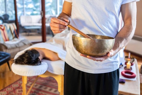 Man holding a bronze sound bowl with a stick, used for sound therapy and sound massages. A