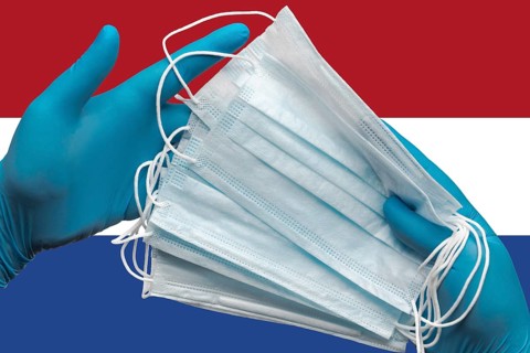 Doctor holds face masks in hands surgical blue gloves on background national flag of Netherlands.