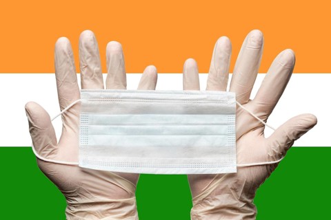 Paramedic holding face mask in two hands in white medical gloves on background flag of India.