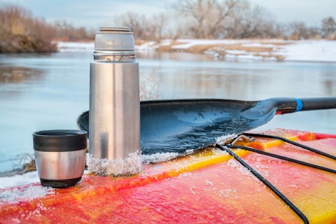 Winter kayaking in Colorado - thermos bottle with hot tea on the icy deck of a red whitewater kayak