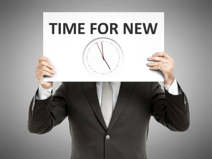 A business man holding a paper in front of his face with time for new and a clock