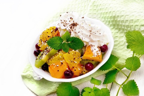Fruit salad with orange, kiwi, cranberries and baked pumpkin, whipped cream, sprinkled with
