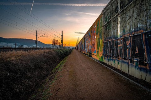 A path along a graffiti-covered wall at sunset, with rails and urban atmosphere, Jena, Thuringia,