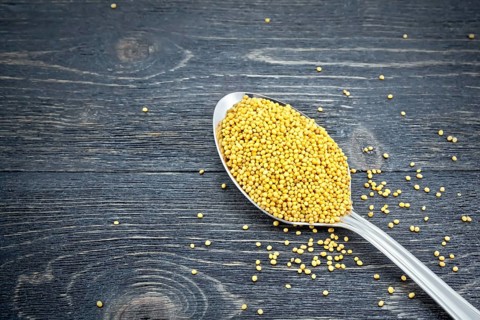 Mustard seeds in a metal spoon on the background of a black wooden board