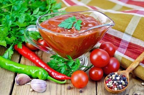 Ketchup in a glass gravy boat, tomatoes, parsley, hot pepper, garlic, napkin on a wooden boards
