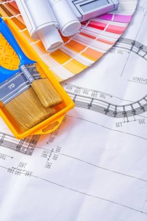Paintbrushes in paint can and rolled blueprints on color pallete