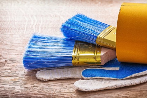 Two paint brushes in roll of duct tape and working gloves on wooden board