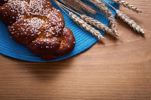 Fresh-baked bun wheat rye ears with blue wattled cover on wooden board food and drink concept