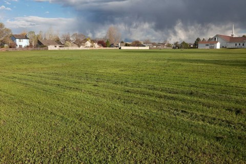 Freshly mowed, large field of grass with residential homes, church and heavy storm clouds in