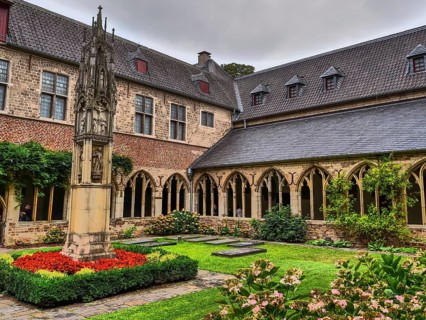 Small monastery courtyard with well-tended garden, Gothic arches and a central stone sculpture,