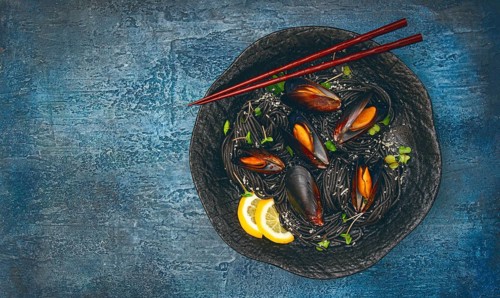 Spaghetti with black squid, black pasta, with boiled mussels, on a black plate, with parsley and