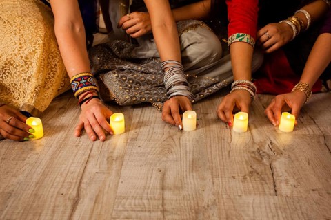 Women's hands holding lighted candles, sitting on floor. Indian holiday Diwali traditions. Closeup