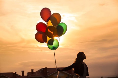 Pretty girl with big colorful balloons walking on the hills near the town. Focus on balloons