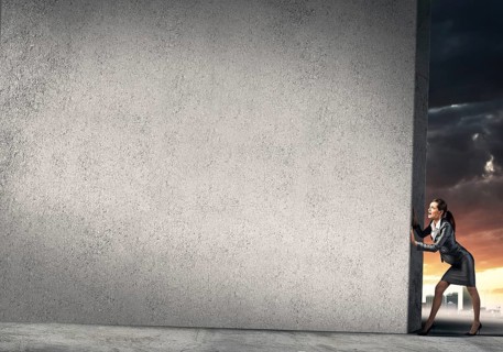 Young businesswoman making effort to move cement wall