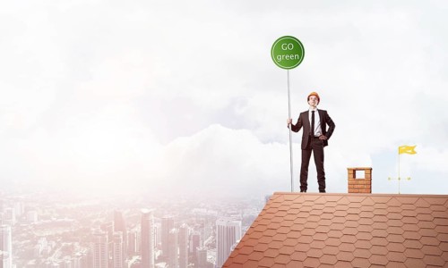 Young caucasian businessman standing on house roof and holding go green sign. Mixed media