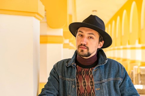 Portrait of a stylish handsome young man with a scarf outdoors. A serious man wearing a hat and a