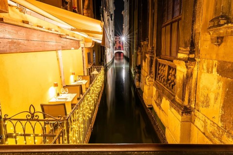 Restaurant tables on a balcony above a canal, night shot, Venice, Italy