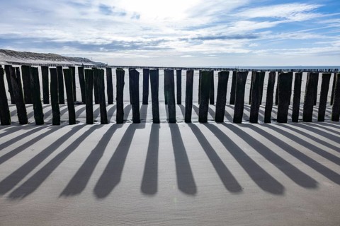 Old, weathered volleyball net on the beach in front of the dunes with sea and blue sky in the