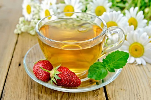 Tea with strawberries in a glass cup, a bouquet of daisies on a background of wooden boards
