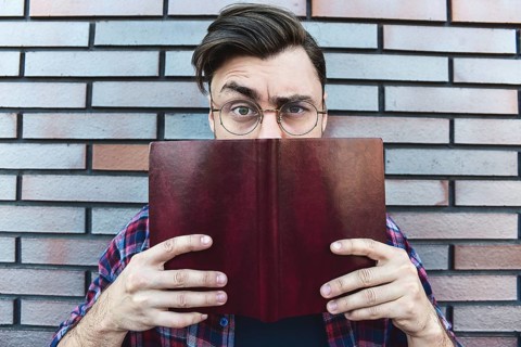 Funny face. Young hipster guy wearing eyeglasses with picked up one browe looking at camera and